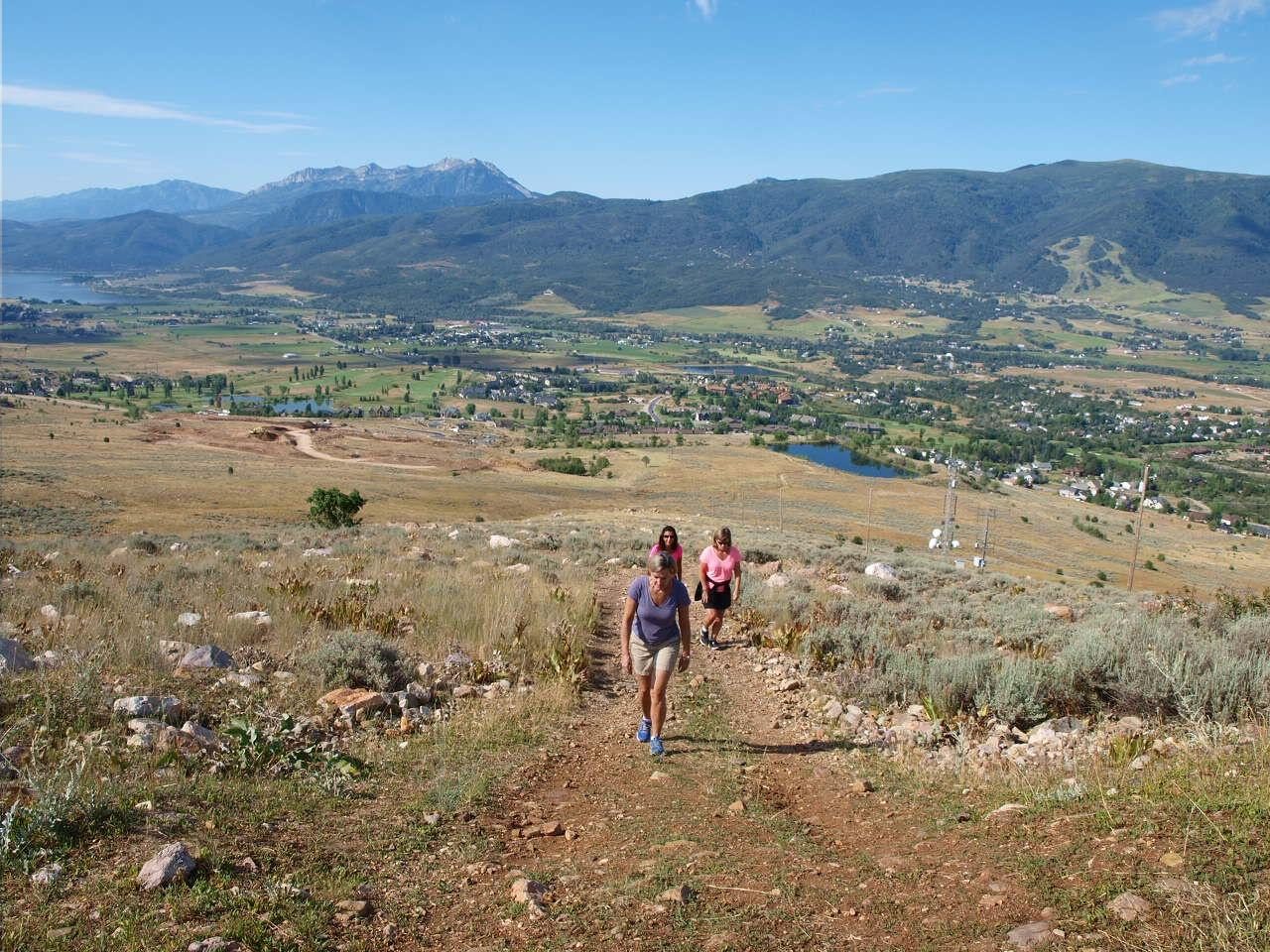 Three walkers climbing a valley trail with Pineview Reservoir and the Wasatch behind