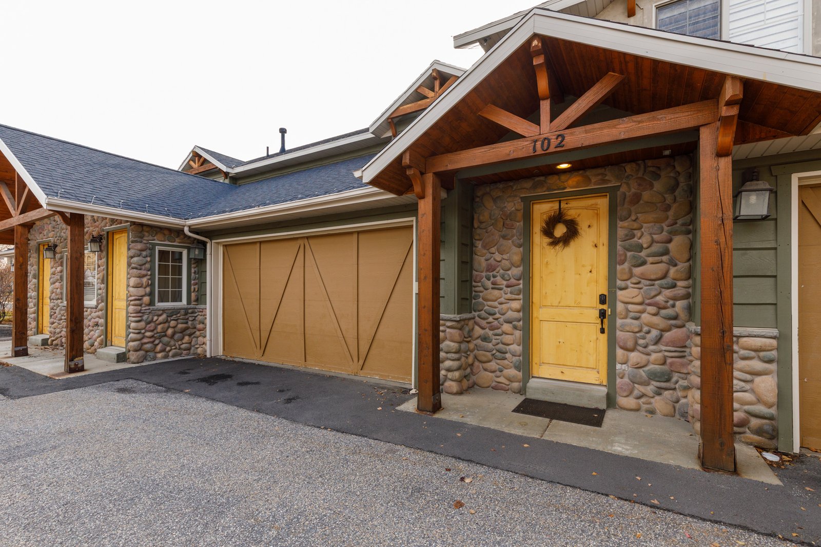 The front door of unit 102 under its timber porch, with river-rock columns and the attached garage