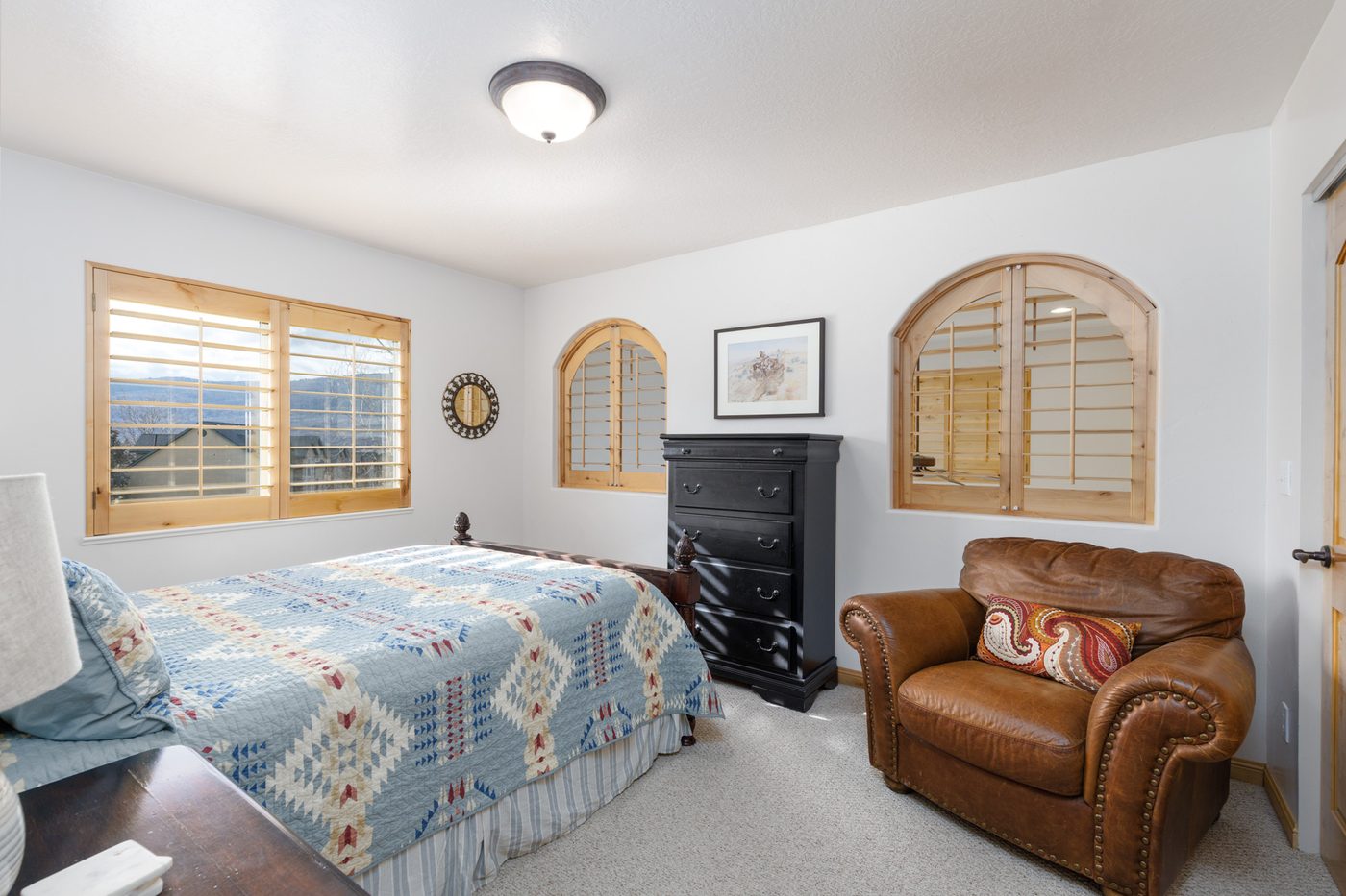 Queen bedroom with arched plantation-shuttered windows and a leather armchair