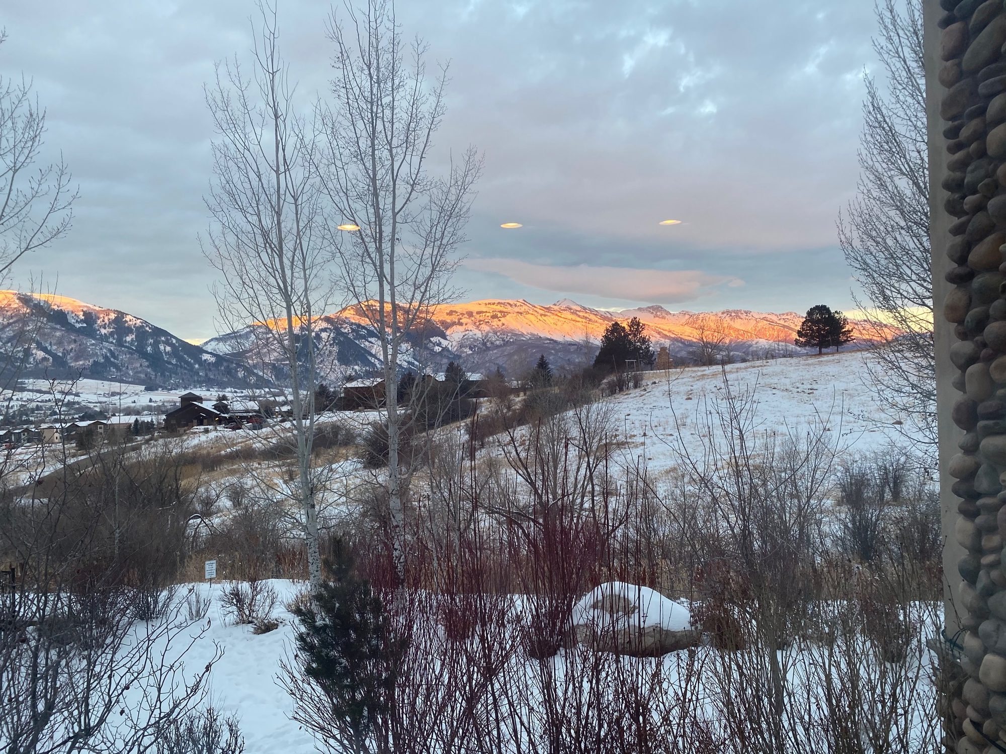 Winter sunset with lenticular clouds over the range, seen past the river-rock column of the porch