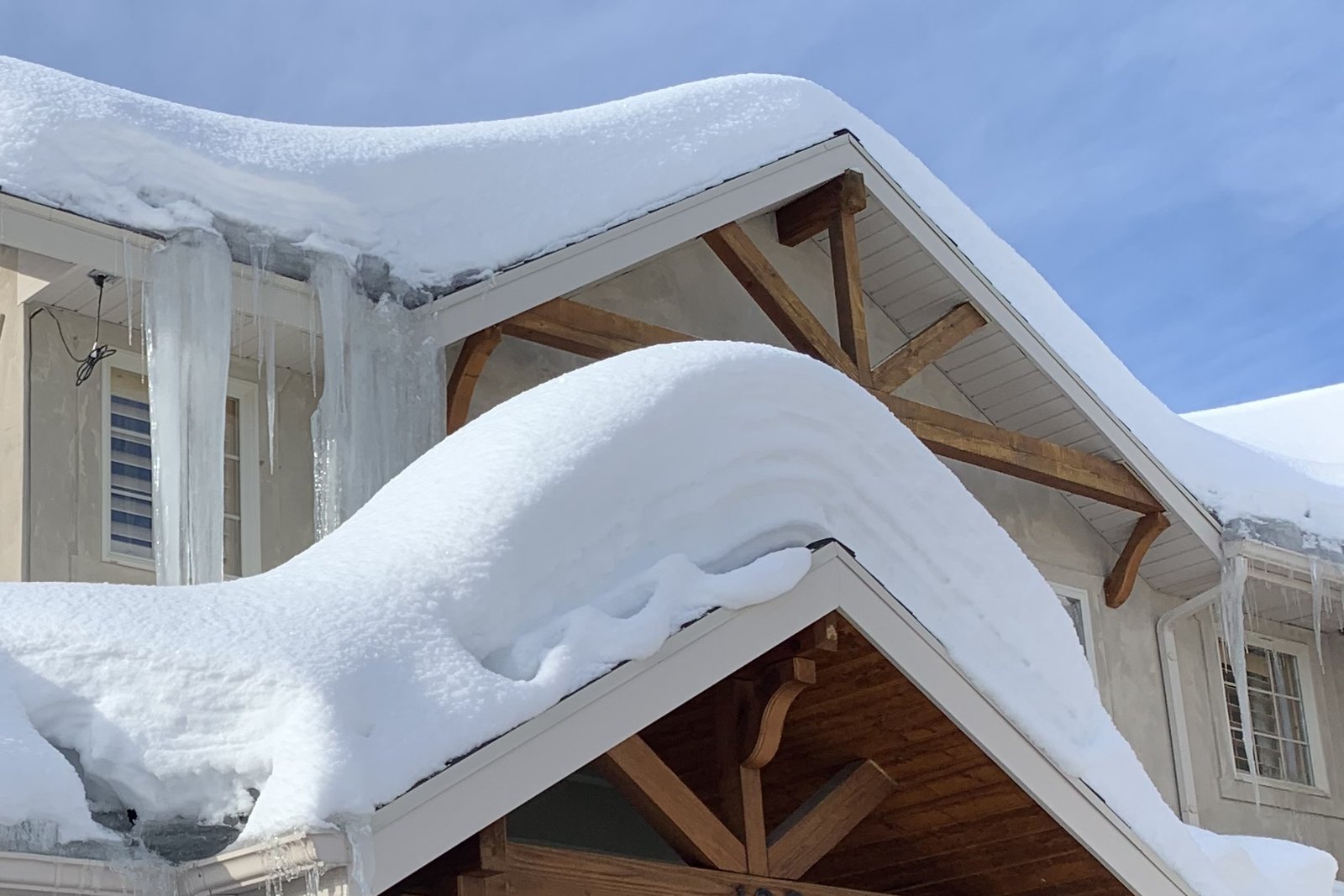 Snow piled deep on the roof and icicles along the eaves above the same front door in midwinter